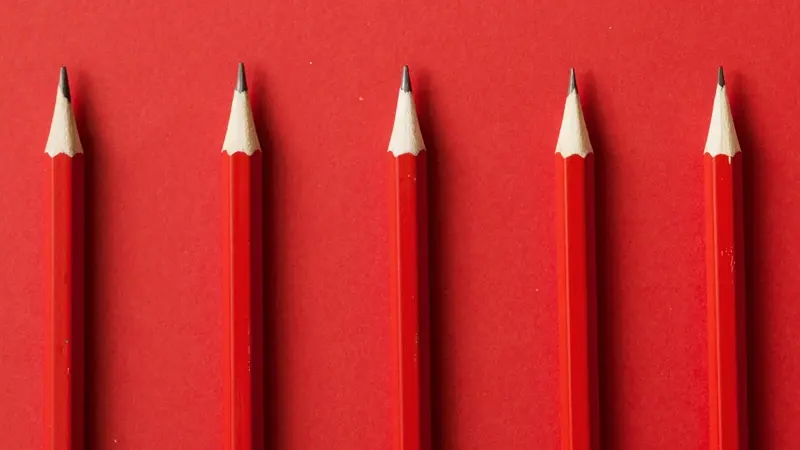 Five red pencils lined up on a red background