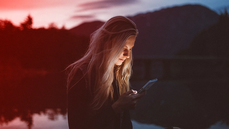 A woman looks at her phone in the middle of nature at sunset.