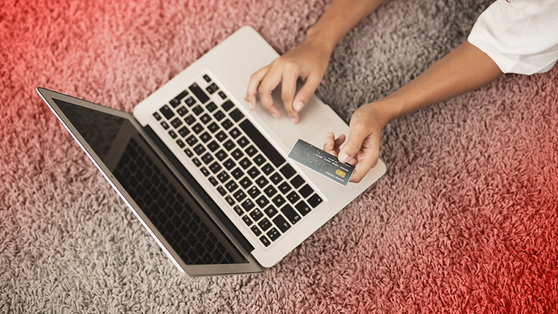 Les mains d'une femme : l'une tient une carte de crédit tandis que l'autre manipule la souris d'un ordinateur portable.
