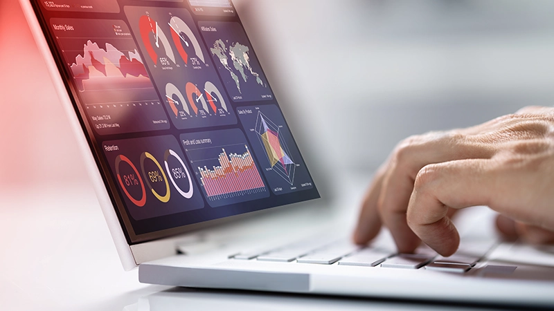 A human hand rests on a laptop, whose screen displays a data analysis.