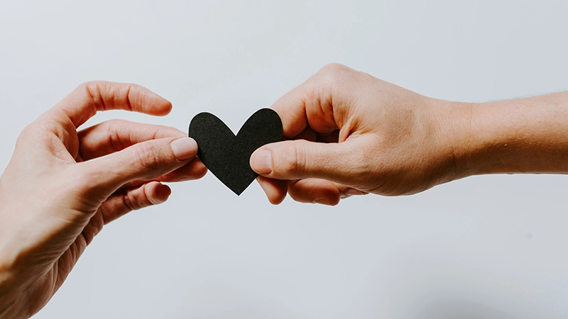 Deux mains tenant un cœur noir en papier