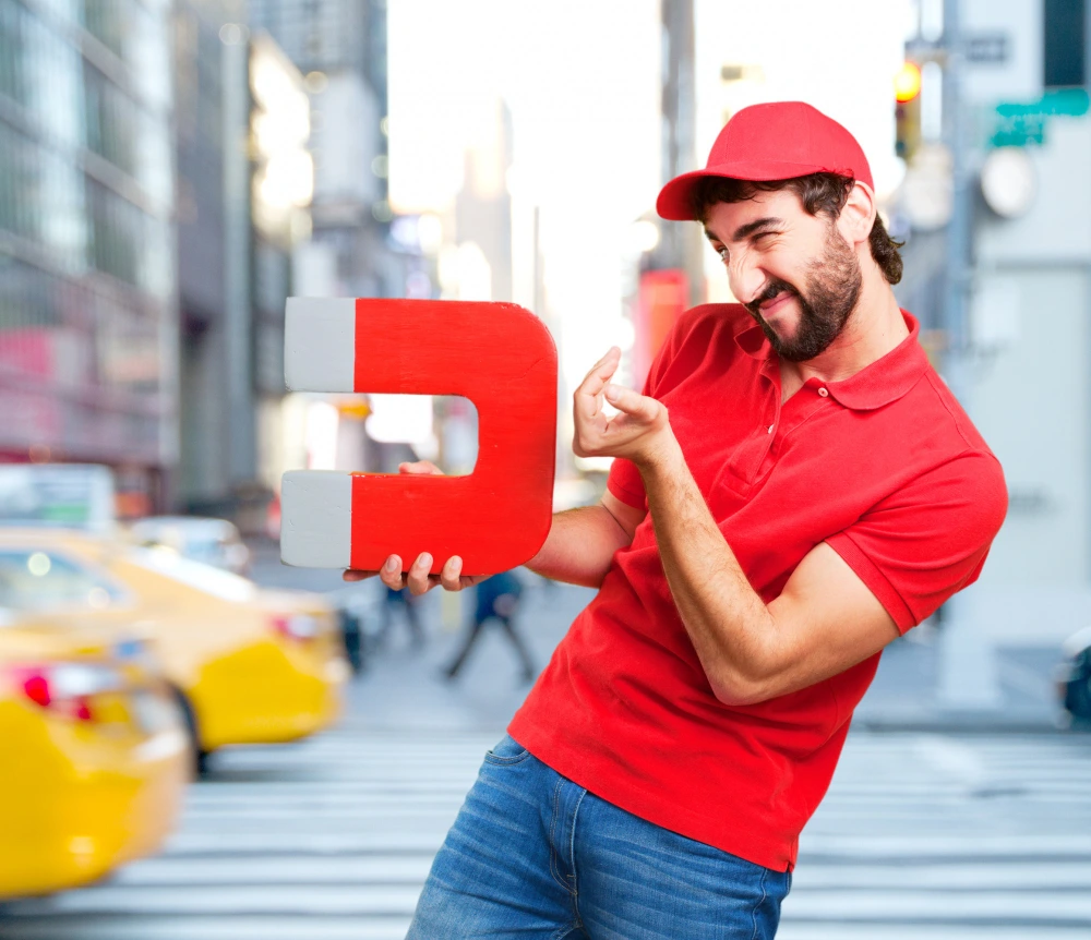 In the heart of a bustling metropolis, a man strives to capture the attention of passers-by. He holds up an imposing red magnet whose powerful magnetic field irresistibly attracts various objects, offering a striking metaphor for his ability to attract new customers.